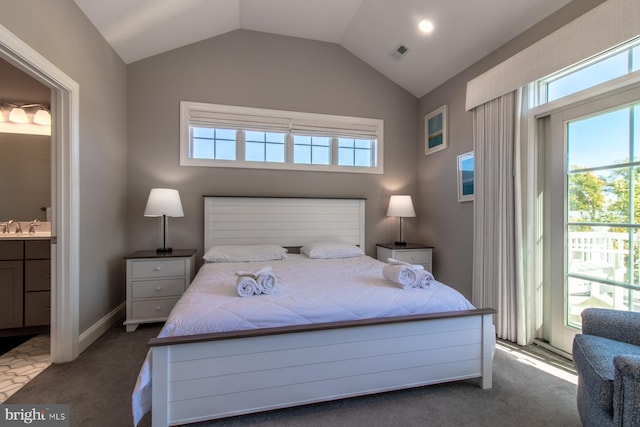 carpeted bedroom featuring sink, vaulted ceiling, multiple windows, and ensuite bath