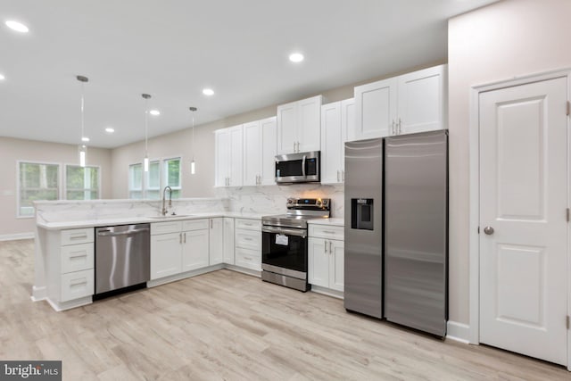 kitchen with stainless steel appliances, light hardwood / wood-style floors, white cabinets, hanging light fixtures, and sink