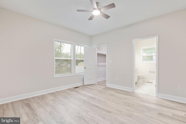 unfurnished bedroom featuring ceiling fan, ensuite bath, light hardwood / wood-style flooring, and a spacious closet