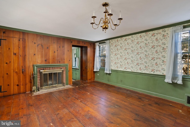 unfurnished living room with ornamental molding, an inviting chandelier, dark hardwood / wood-style floors, and a fireplace