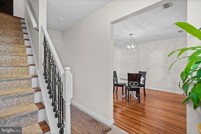 stairs with hardwood / wood-style floors and a notable chandelier