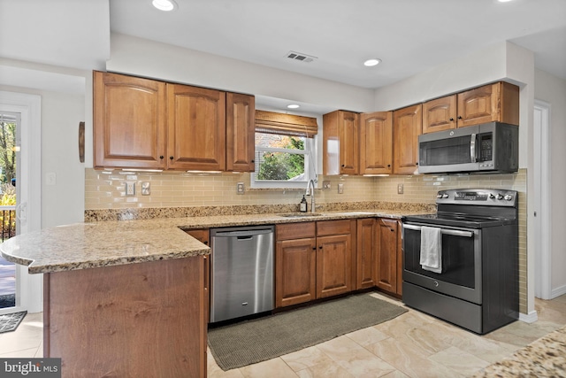 kitchen with sink, decorative backsplash, appliances with stainless steel finishes, light stone counters, and kitchen peninsula