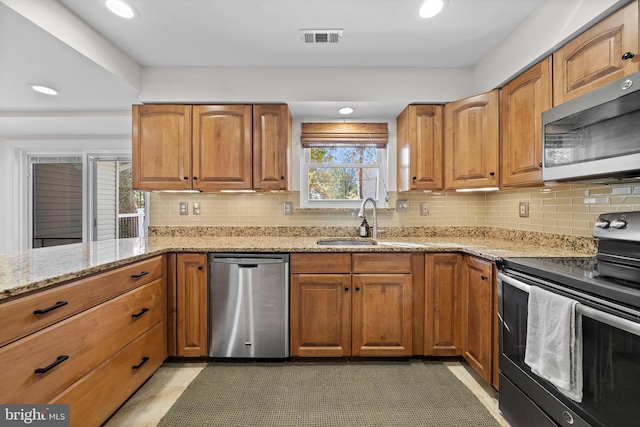 kitchen featuring appliances with stainless steel finishes, tasteful backsplash, light stone counters, and sink