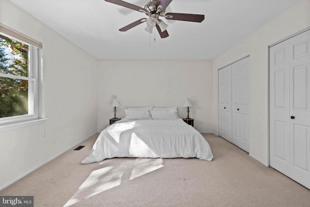 carpeted bedroom featuring ceiling fan and multiple closets