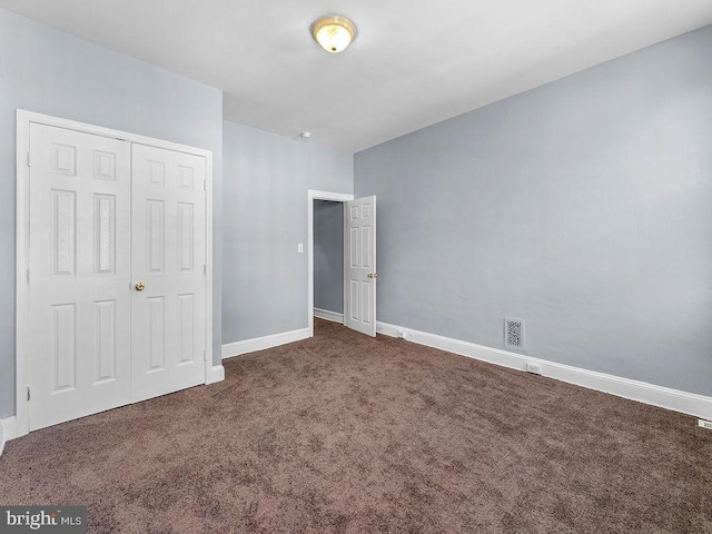 unfurnished bedroom with dark colored carpet and a closet