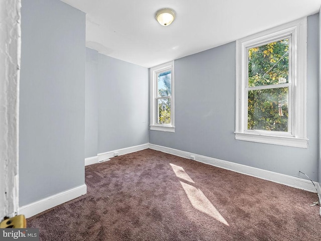 unfurnished room with dark colored carpet and a wealth of natural light