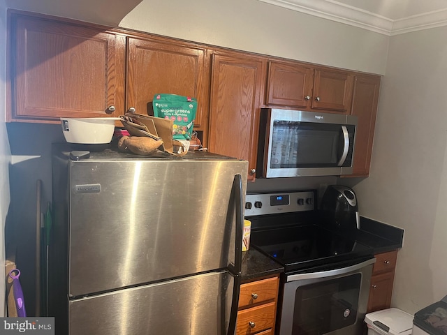kitchen with brown cabinetry, stainless steel appliances, crown molding, and dark countertops