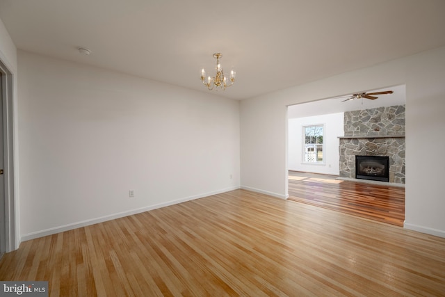 unfurnished living room featuring a stone fireplace, light wood-type flooring, and ceiling fan with notable chandelier