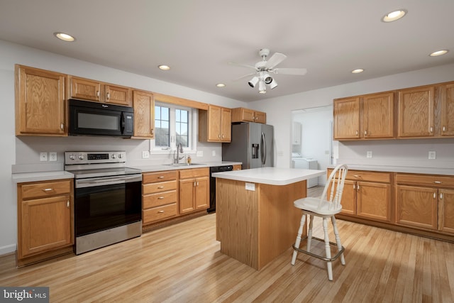 kitchen featuring black appliances, a kitchen island, sink, light hardwood / wood-style floors, and a breakfast bar