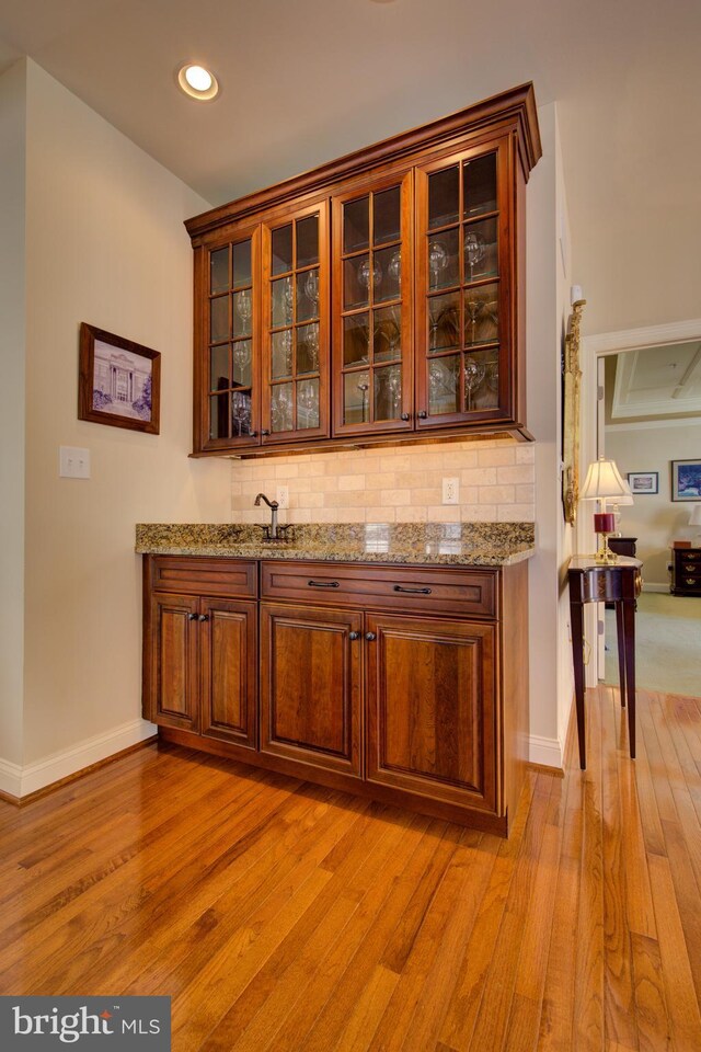 bar featuring light wood-type flooring, tasteful backsplash, and light stone countertops