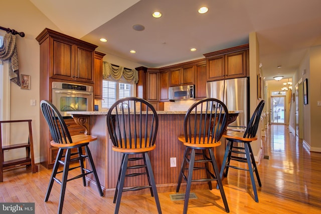 kitchen with stainless steel appliances, light hardwood / wood-style floors, a breakfast bar, light stone countertops, and decorative backsplash