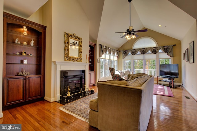 living room with high vaulted ceiling, wood-type flooring, ceiling fan, and a high end fireplace