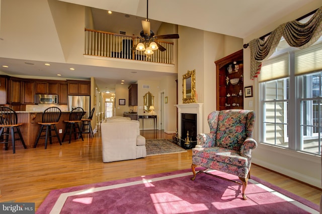 living room featuring a high ceiling, ceiling fan, and light hardwood / wood-style flooring