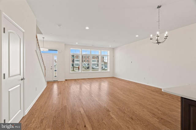 unfurnished living room featuring baseboards, recessed lighting, a chandelier, and light wood-type flooring