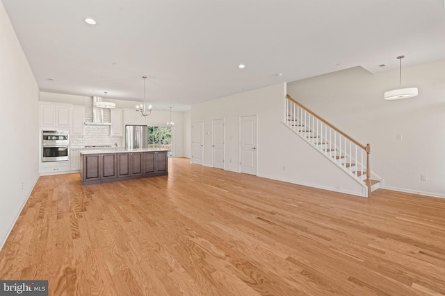 unfurnished living room with light wood finished floors, a notable chandelier, stairway, baseboards, and recessed lighting
