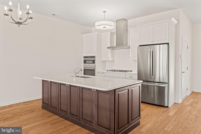 kitchen with wall chimney exhaust hood, dark brown cabinetry, pendant lighting, light wood-type flooring, and appliances with stainless steel finishes