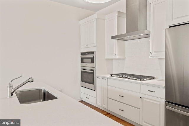 kitchen with stainless steel appliances, a sink, wood finished floors, wall chimney range hood, and light countertops