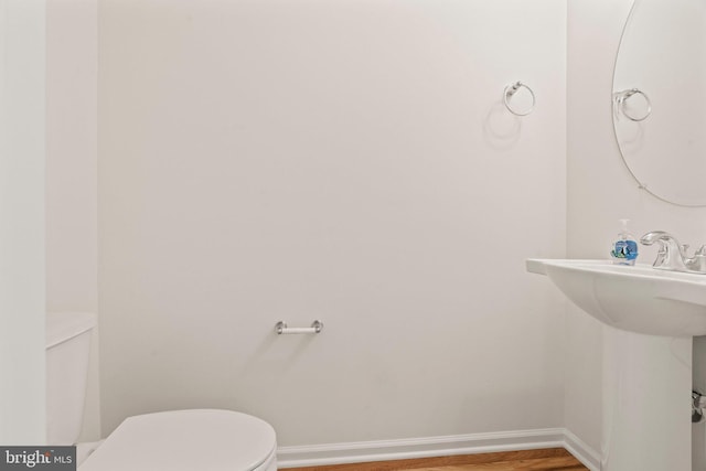 half bath with toilet, wood finished floors, and baseboards
