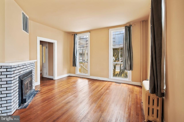 unfurnished living room with radiator heating unit, light hardwood / wood-style floors, and a brick fireplace