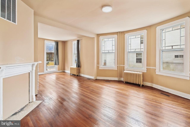 unfurnished living room with radiator, a healthy amount of sunlight, and light hardwood / wood-style flooring