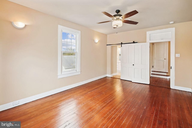 unfurnished bedroom with a barn door, hardwood / wood-style flooring, and ceiling fan