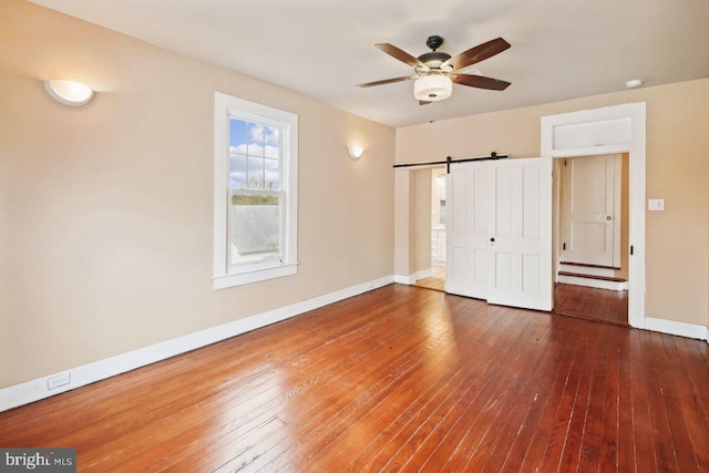 205 Walnut St, Pocomoke City, MD 21851 - unfurnished bedroom with wood-type flooring, baseboards, a barn door, and a ceiling fan