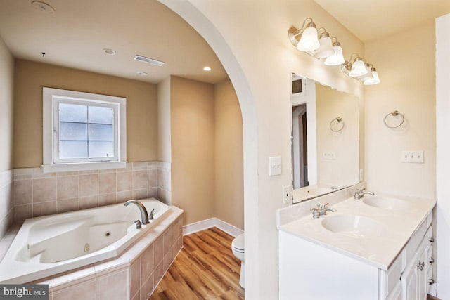 bathroom with hardwood / wood-style floors, tiled bath, vanity, and toilet