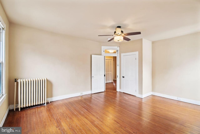 unfurnished room featuring hardwood / wood-style floors, ceiling fan, and radiator heating unit