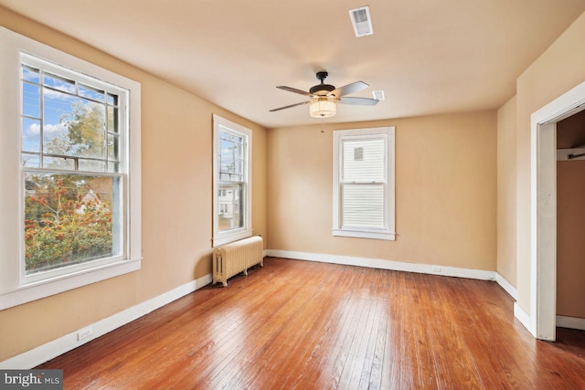 empty room featuring radiator heating unit, light hardwood / wood-style floors, ceiling fan, and plenty of natural light