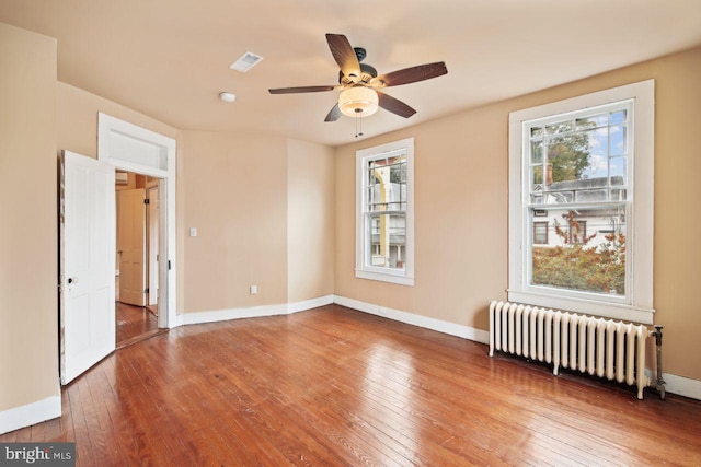 spare room featuring radiator heating unit, hardwood / wood-style flooring, and ceiling fan