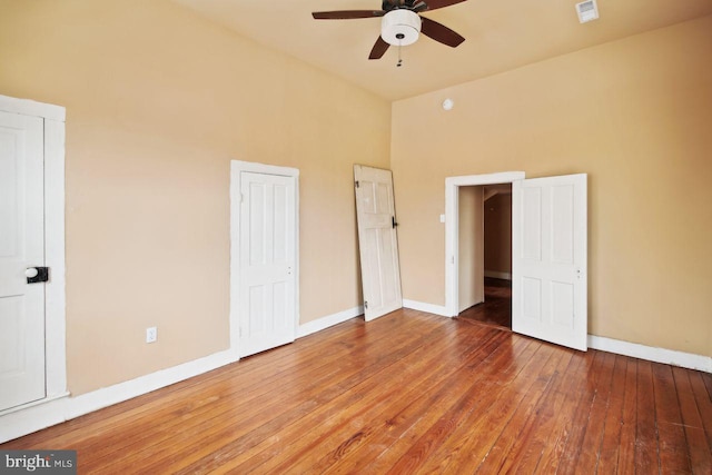 unfurnished bedroom featuring wood-type flooring, ceiling fan, and a towering ceiling