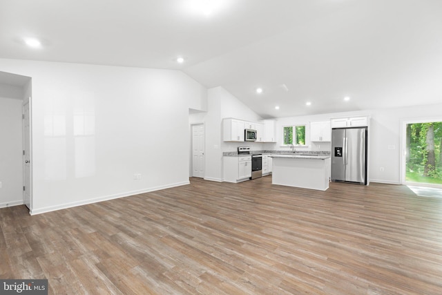 kitchen with stainless steel appliances, vaulted ceiling, a center island, light wood-type flooring, and white cabinetry