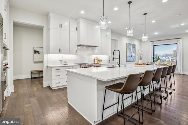 kitchen with white cabinetry, a kitchen breakfast bar, dark hardwood / wood-style flooring, a large island with sink, and pendant lighting