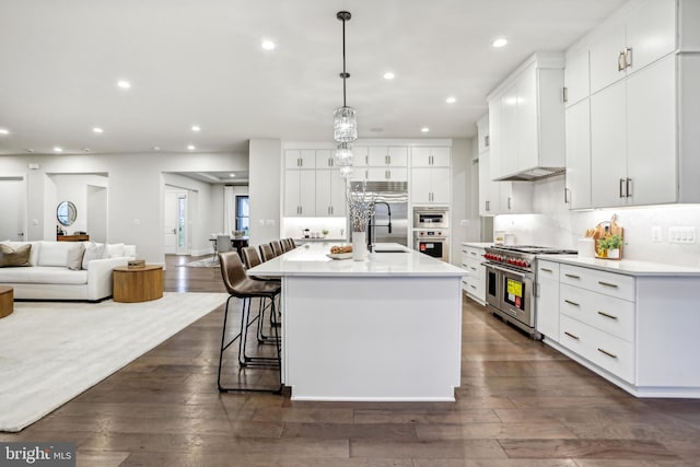 kitchen featuring high end appliances, dark hardwood / wood-style floors, an island with sink, decorative light fixtures, and white cabinetry