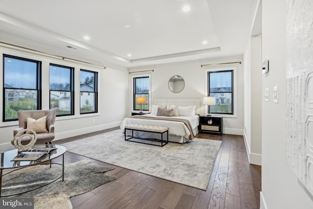 bedroom with dark wood-type flooring, a tray ceiling, and multiple windows