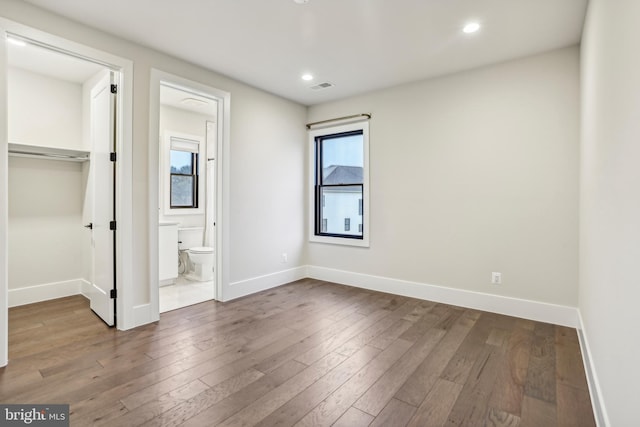 unfurnished bedroom featuring ensuite bath and hardwood / wood-style floors