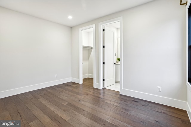 unfurnished bedroom featuring a spacious closet, dark wood-type flooring, and a closet