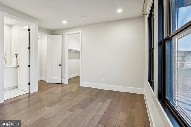 unfurnished bedroom with a walk in closet, a closet, ensuite bath, and light hardwood / wood-style floors