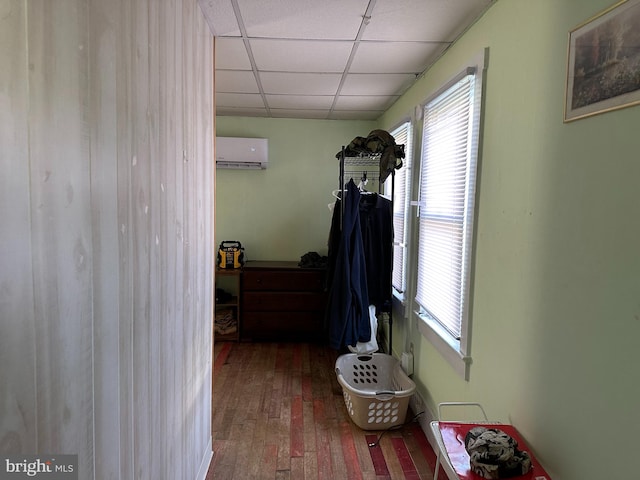 hallway with an AC wall unit, a paneled ceiling, and hardwood / wood-style floors