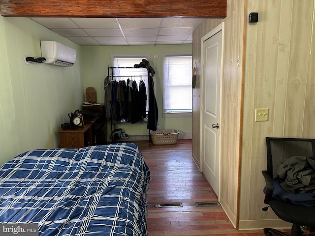 bedroom featuring a wall unit AC, a paneled ceiling, and hardwood / wood-style flooring