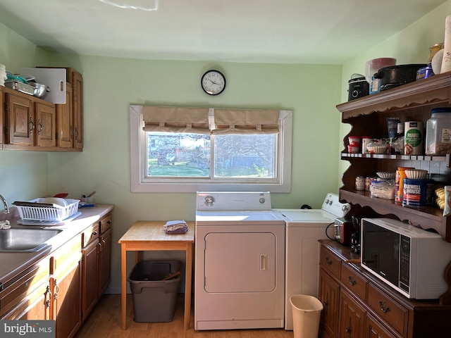 laundry area with light hardwood / wood-style floors, washer and clothes dryer, and sink