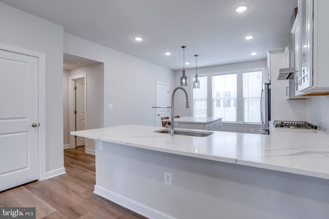 kitchen with sink, light stone countertops, hanging light fixtures, white cabinets, and light wood-type flooring