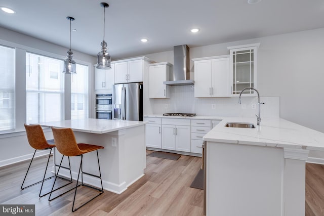 kitchen featuring light wood-type flooring, appliances with stainless steel finishes, sink, white cabinets, and wall chimney exhaust hood