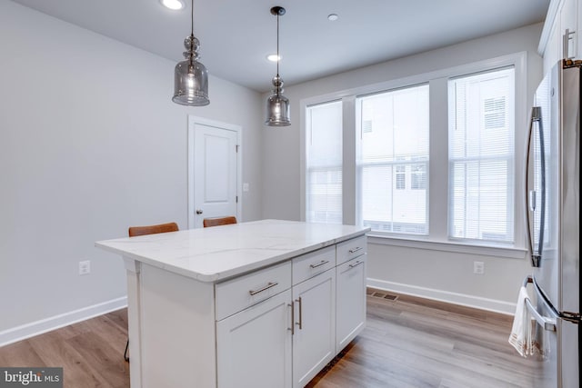 kitchen with light stone counters, a center island, white cabinets, light wood-type flooring, and stainless steel fridge