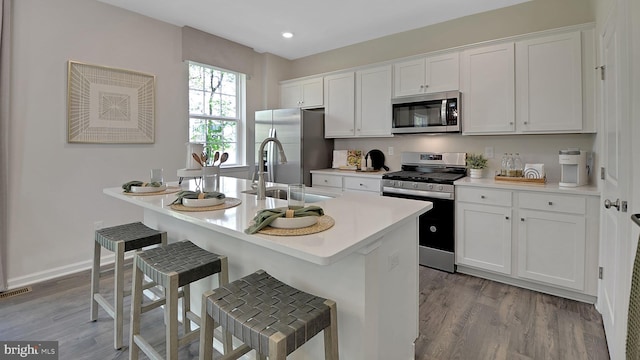 kitchen featuring white cabinetry, sink, stainless steel appliances, light hardwood / wood-style flooring, and a kitchen bar