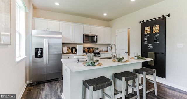 kitchen with appliances with stainless steel finishes, a breakfast bar, dark wood-type flooring, a center island with sink, and white cabinets