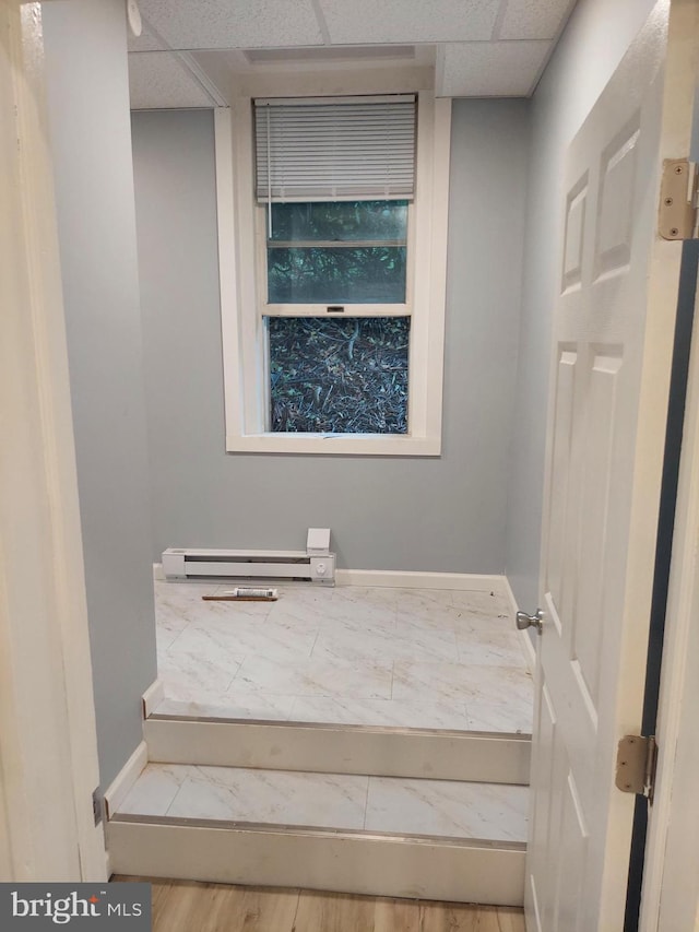 stairway with a baseboard heating unit, a paneled ceiling, and hardwood / wood-style flooring