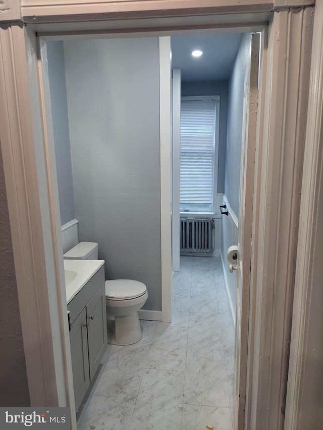 bathroom featuring vanity, radiator heating unit, and toilet