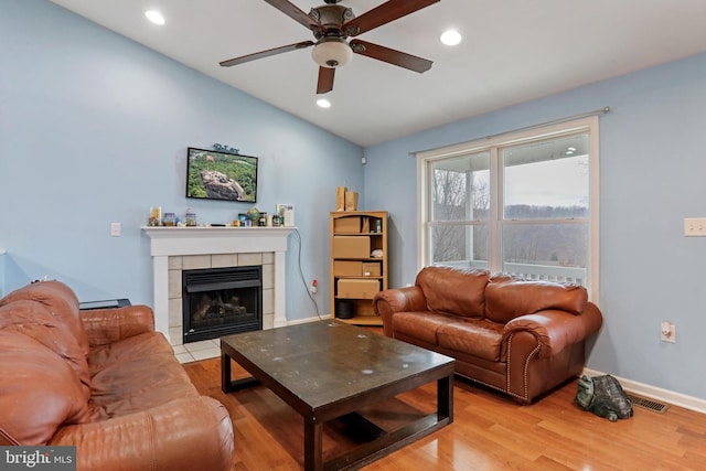 living room featuring ceiling fan, lofted ceiling, a fireplace, and light hardwood / wood-style flooring