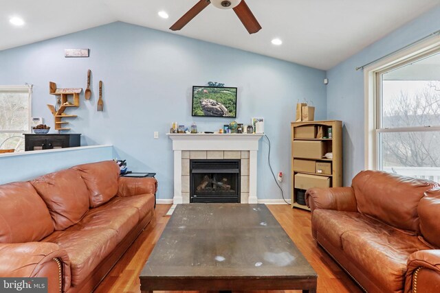 living room with hardwood / wood-style floors, ceiling fan, a tiled fireplace, and vaulted ceiling